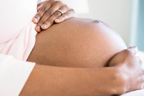 A pregnant black woman with her hands on her stomach